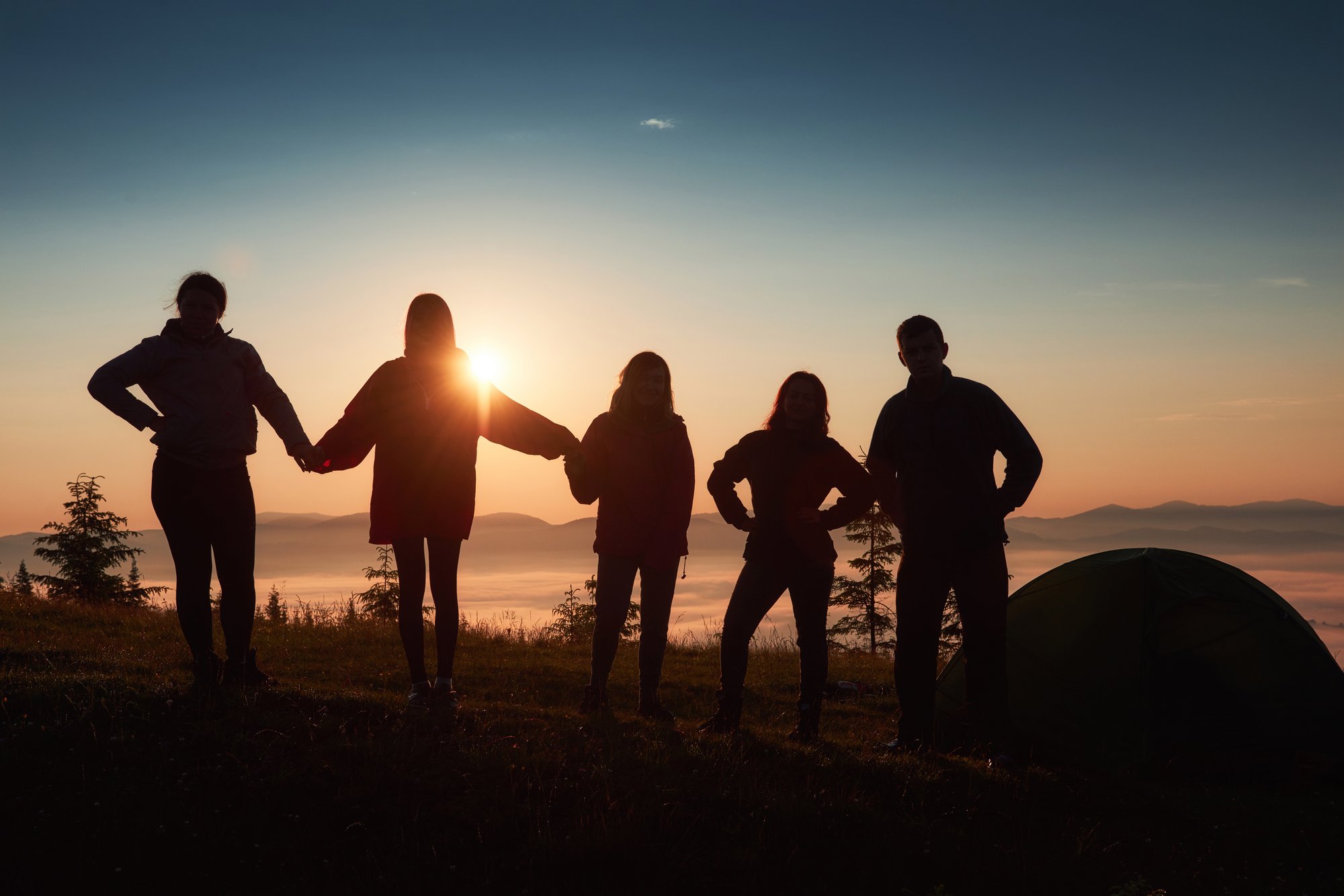 une-silhouette-de-gens-du-groupe-s-amuse-au-sommet-de-la-montagne-pres-de-la-tente-pendant-le-coucher-du-soleil une-silhouette-de-gens-du-groupe-s-amuse-au-sommet-de-la-montagne-pres-de-la-tente-pendant-le-coucher-du-soleil